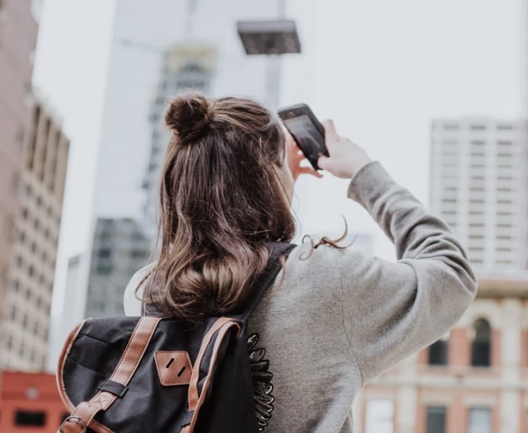 Ein Mädchen trägt einen Rucksack und macht mit ihrer Handykamera Fotos von Gebäuden
