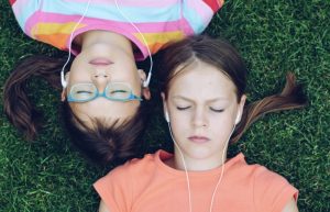 Zwei junge Mädchen liegen auf dem Rasen und hören Musik