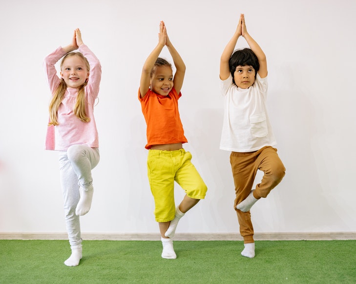 Drei Kinder machen eine Yogaübung.