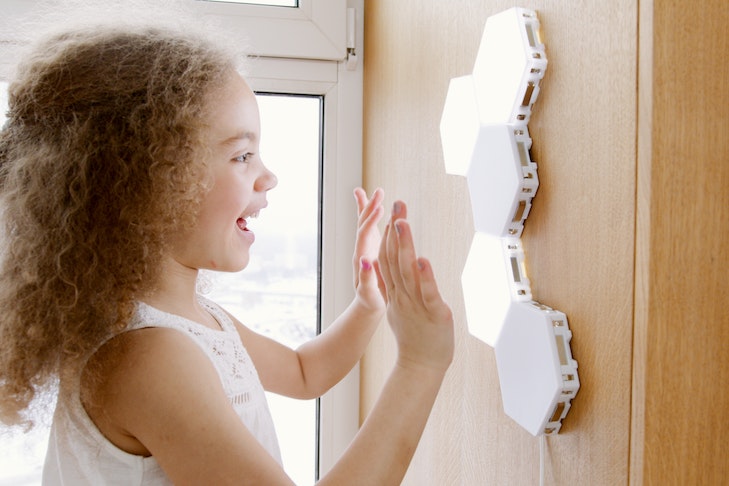 Ein Mädchen steht vor LED-Panels, die an einer Wand befestigt sind und freut sich.