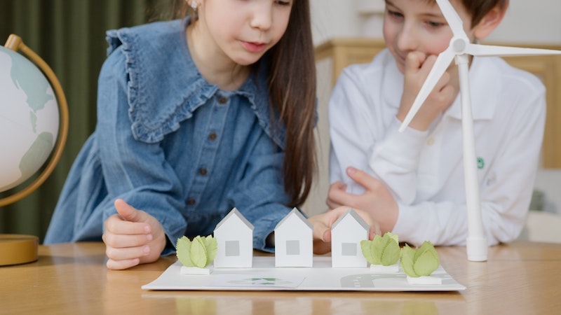Ein Mädchen und ein Junge sitzen vor 3D-Modellen von Häusern und einer Windturbine